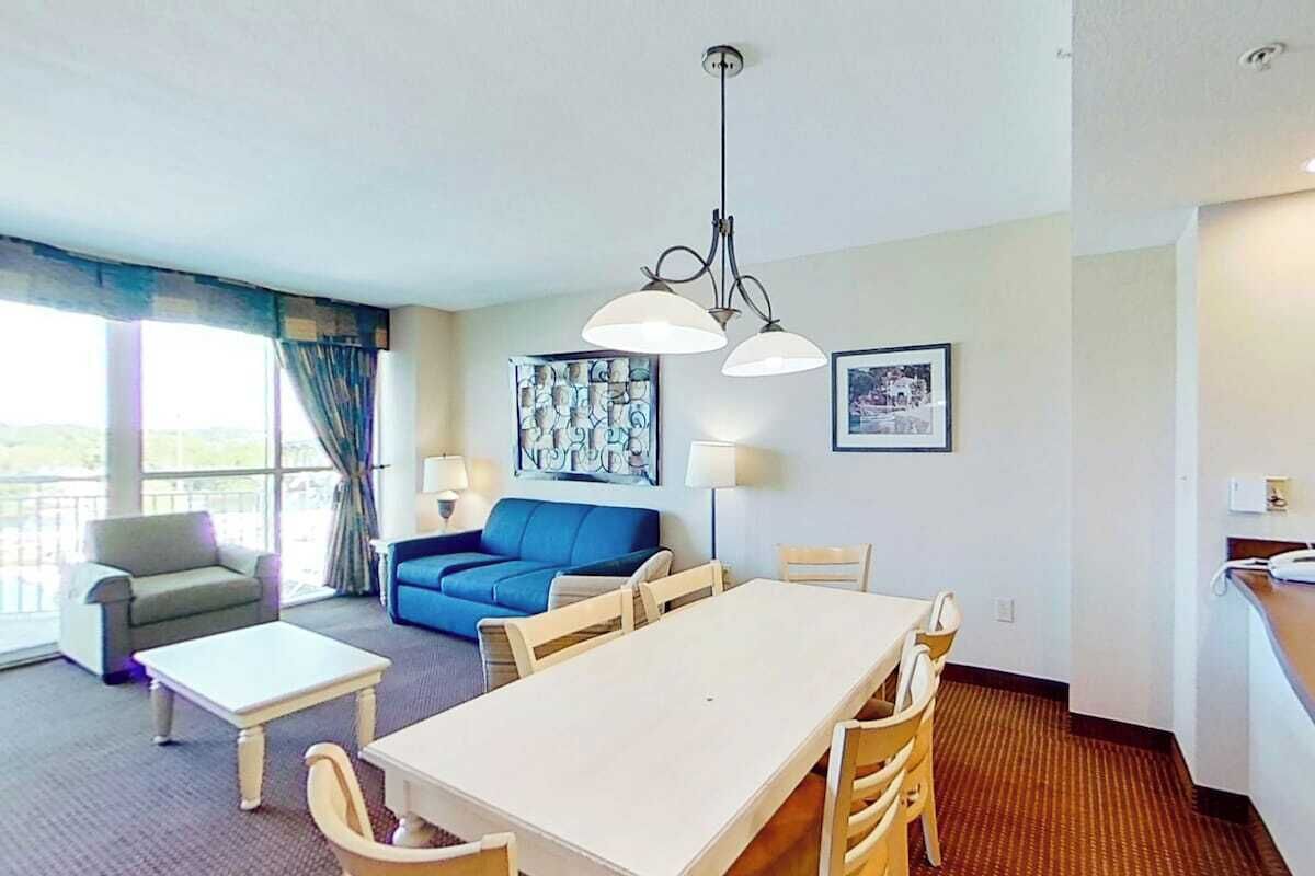 Une chambre d’hôtel équipée d’une table à manger, de chaises, d’un canapé, d’une table basse et d’une grande fenêtre avec des rideaux.