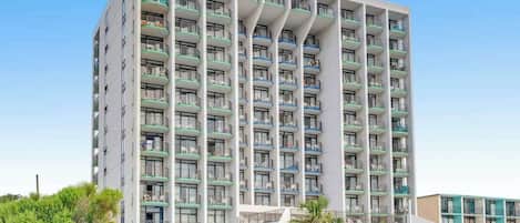A multi-story hotel with balconies, a central staircase, and a pool area.
