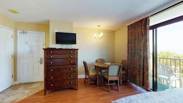 Quarto de hotel com cômoda de madeira, televisão na parede, mesa de jantar com cadeiras e varanda com vista.