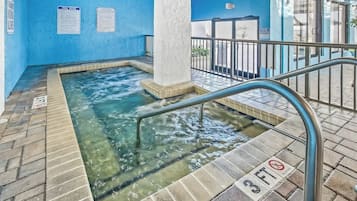 Uma área de hidromassagem com água cristalina, um corrimão de metal e uma placa de 'Proibido Mergulhar'.