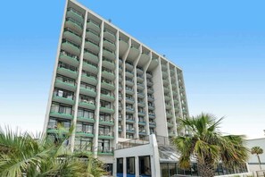 Un hotel de varios pisos con balcones, una entrada cubierta y palmeras.