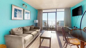 A room with a sofa, a dining table, chairs, a TV, and a balcony with a view. - Ocean Park Resort 0522 (Myrtle Beach)