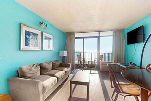 Ein Zimmer mit einer Couch, einem Esstisch, Stühlen, einem Fernseher und einem Balkon mit Blick.