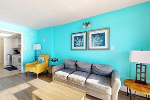 Sala de estar con sofá, una mesa de centro, un sillón amarillo y una lámpara. En la pared, hay cuadros enmarcados.