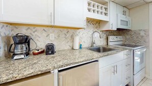A kitchen with white cabinets, a granite countertop, a coffee maker, a toaster, a microwave, and a sink. - Ocean Park Resort 0522 (Myrtle Beach)