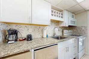 Eine Küche mit weißen Schränken, einer Granit-Arbeitsplatte, einer Kaffeemaschine, einem Toaster, einer Mikrowelle und einem Spülbecken.