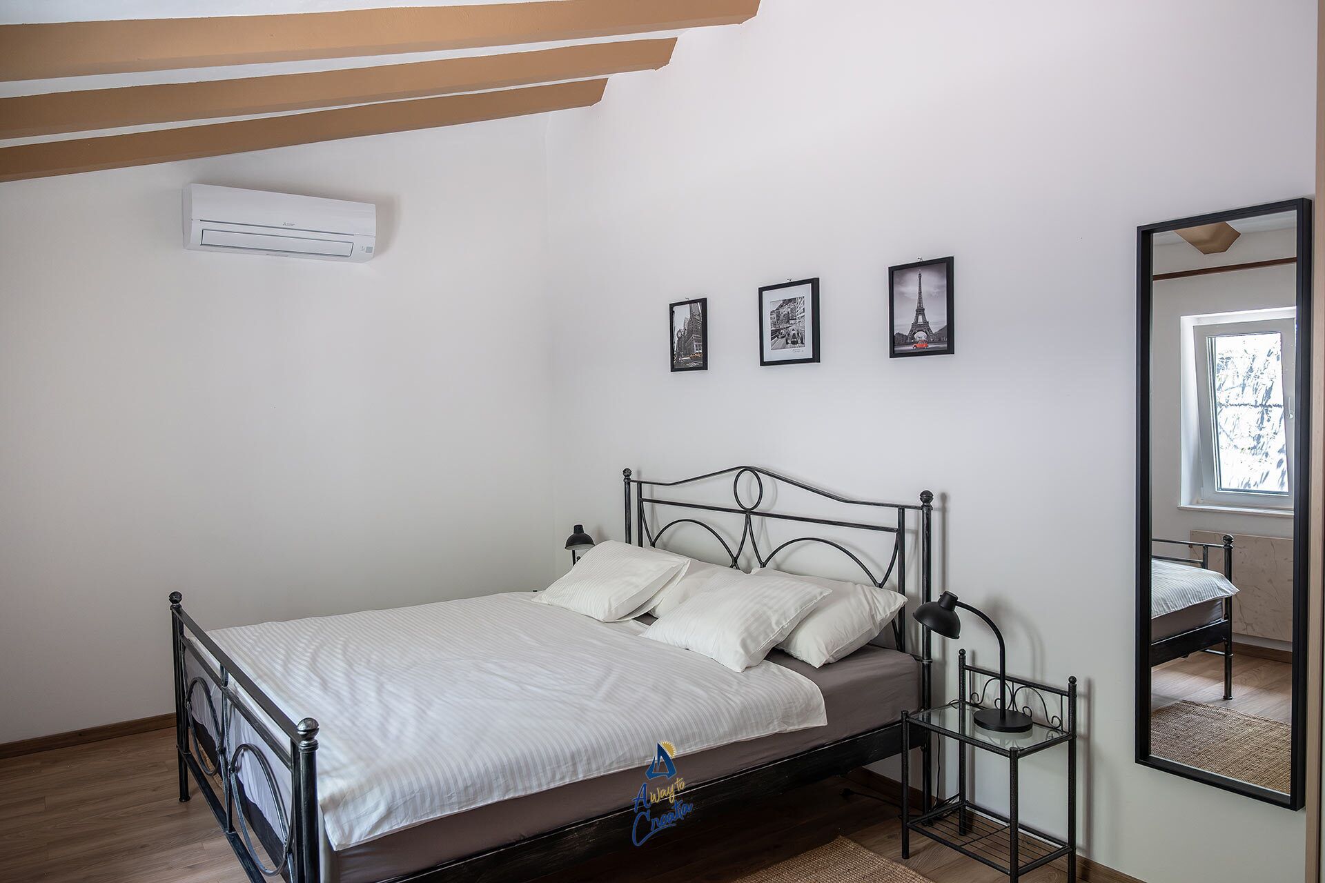 Un dormitorio con cama, lámpara de noche, espejo y tres cuadros en la pared.