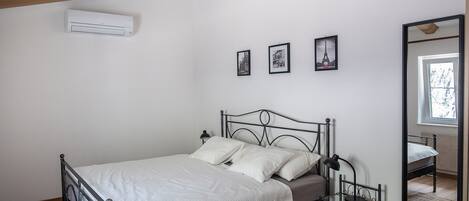 A bedroom with a bed, a bedside lamp, a mirror, and three framed pictures on the wall.