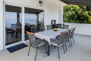 Une terrasse extérieure avec une table et des chaises, un barbecue et une vue sur la mer.