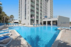 A swimming pool with lounge chairs and a multi-story building in the background. - Ocean Park Resort 0524 (Myrtle Beach)