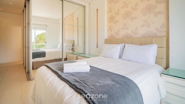 A modern bedroom with a large bed, a glass partition, a bedside table, and a floral wallpaper.