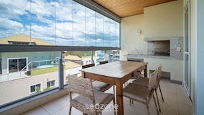 A balcony with a wooden table and wicker chairs, a stone fireplace, and a view of neighboring buildings.