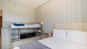 Una habitación de hotel con literas, una mesita de noche con lámpara, un televisor y una cama grande con almohadas.
