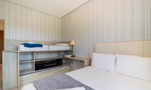 Una habitación de hotel con literas, una mesita de noche con lámpara, un televisor y una cama grande con almohadas.