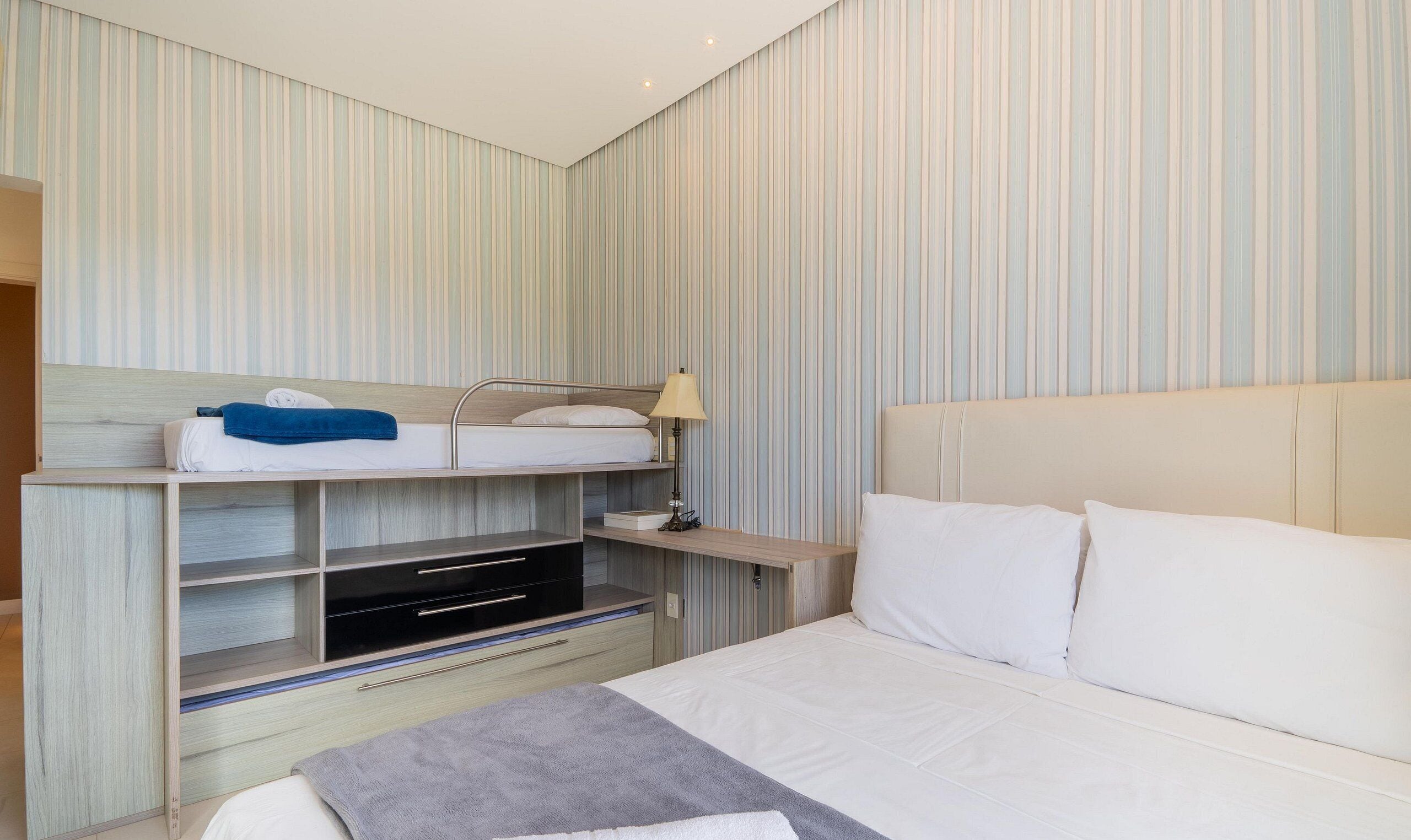 Una habitación de hotel con literas, una mesita de noche con lámpara, un televisor y una cama grande con almohadas.