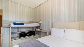 Una habitación de hotel con literas, una mesita de noche con lámpara, un televisor y una cama grande con almohadas.