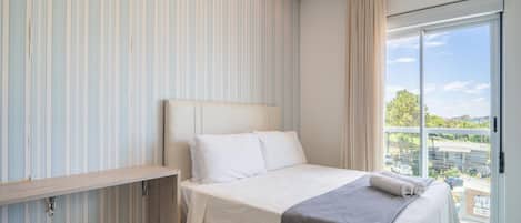 A modern bedroom with a bed, a bedside table, and a view of the outside through a large window.