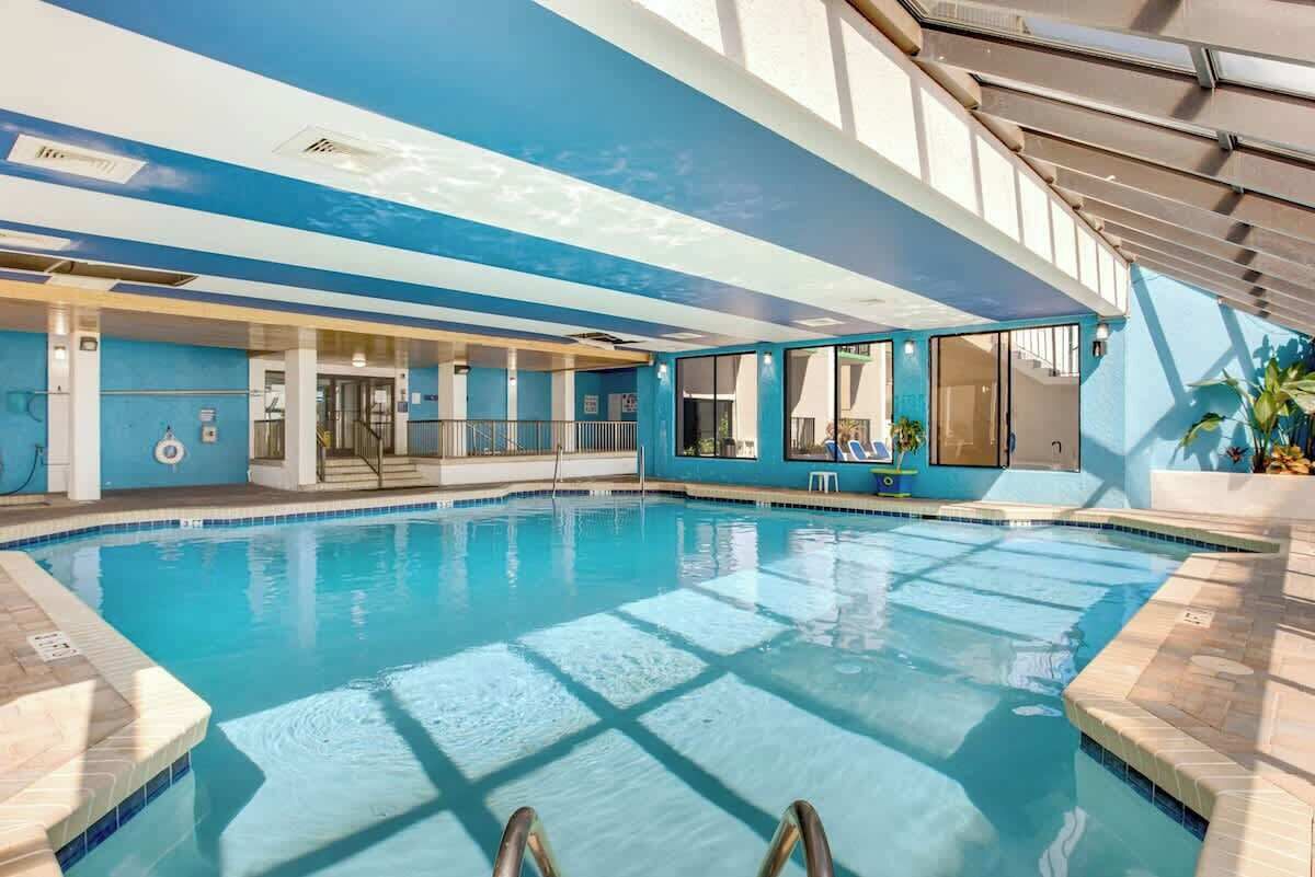 An indoor swimming pool with clear blue water, a tiled floor, and a view of the sky through the ceiling.