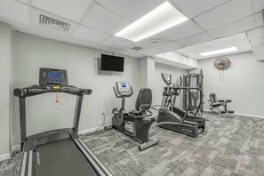 Ein Fitnessstudio mit Cardio-Geräten, Krafttrainingsmaschinen und einem Fernseher an der Wand.