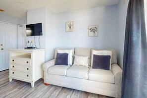 A room with a white dresser, a beige sofa with cushions, a flat-screen TV mounted on the wall, and two framed pictures. - Ocean Park Resort 0924 (Myrtle Beach)