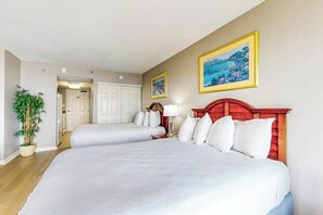 Ein Hotelzimmer mit zwei Betten, einem Blumentopf und zwei gerahmten Bildern an der Wand.