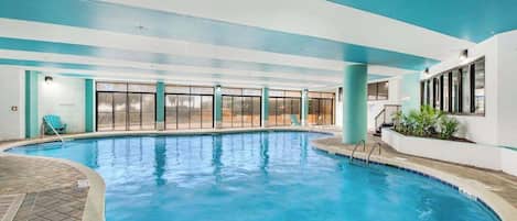 Una piscina interior con paredes de vidrio transparente, suelo de baldosas y techo azul.
