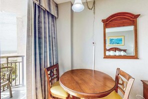 A round wooden dining table with four chairs, a hanging light fixture, a mirror with a picture, and a balcony with a view. - The Patricia Grand 0528 (Myrtle Beach)