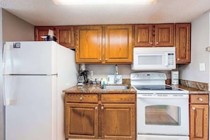 A compact kitchen with wooden cabinets, a white refrigerator, a microwave, a stove, and a sink. - The Patricia Grand 0528 (Myrtle Beach)