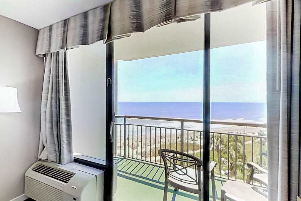 A balcony with a view of the sea, a chair, and an air conditioning unit.