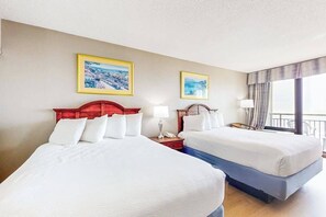A hotel room with two beds, a red headboard, a nightstand with a lamp, and a window with curtains. - The Patricia Grand 0528 (Myrtle Beach)