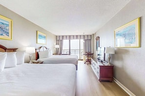 A hotel room with two beds, a desk, a chair, a dresser, and a large window with curtains. - The Patricia Grand 0528 (Myrtle Beach)