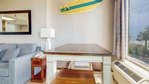 Ein Zimmer mit Holztisch, einer Couch, einem Spiegel, einer Surfbret-Dekoration und Meerblick durch ein Fenster.