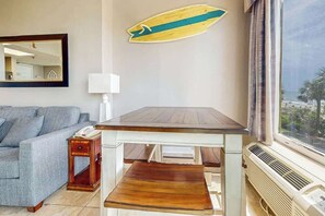 Ein Zimmer mit Holztisch, einer Couch, einem Spiegel, einer Surfbret-Dekoration und Meerblick durch ein Fenster.