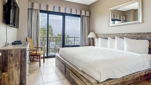 Ein Hotelzimmer mit einem großen Bett, einem Schreibtisch, einem Sessel, einem Fernseher und einem Balkon mit Blick.