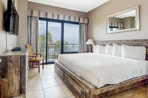 Ein Hotelzimmer mit einem großen Bett, einem Schreibtisch, einem Sessel, einem Fernseher und einem Balkon mit Blick.