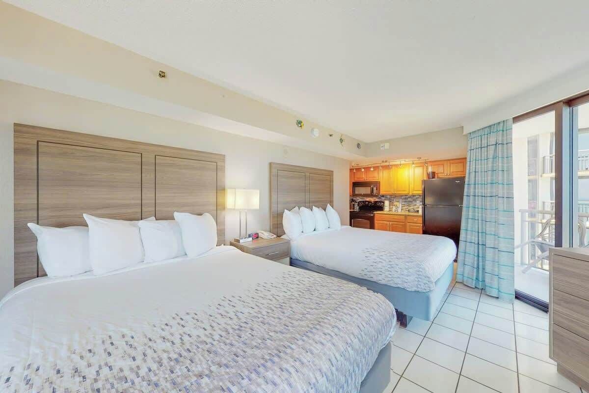 Quarto de hotel com duas camas, uma cozinha compacta e varanda com vista.