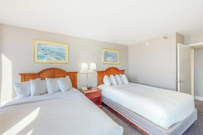 Ein Hotelzimmer mit zwei Einzelbetten, einem Nachttisch mit Lampe und zwei gerahmten Bildern an der Wand.