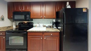 A kitchen with wooden cabinets, a black microwave, a stove, and a refrigerator. - The Patricia Grand 0624 (Myrtle Beach)