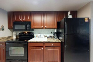 A kitchen with wooden cabinets, a black microwave, a stove, and a refrigerator. - The Patricia Grand 0624 (Myrtle Beach)