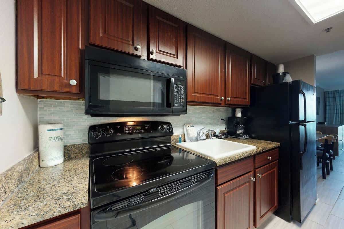 A kitchen with dark wooden cabinets, a black microwave, a stove, and a refrigerator.