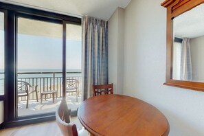 A room with a wooden table and chairs, a large window with a view of the beach, and a balcony with outdoor furniture. - The Patricia Grand 0628 (Myrtle Beach)