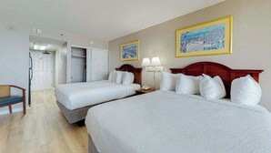 A hotel room with two beds, a desk, and a chair. There are two paintings on the wall. - The Patricia Grand 0628 (Myrtle Beach)