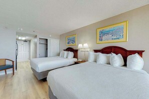 A hotel room with two beds, a desk, and a chair. There are two paintings on the wall. - The Patricia Grand 0628 (Myrtle Beach)