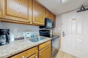 A kitchen with wooden cabinets, a stainless steel sink, a black microwave, and a dishwasher. - The Patricia Grand 0628 (Myrtle Beach)