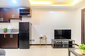 Una cocina moderna con armarios de madera oscura, un refrigerador negro, una pequeña mesa redonda con un florero y un televisor de pantalla plana sobre un mueble.