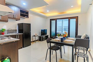A modern kitchen with a dining area, built-in cabinets, a refrigerator, and a television. - Comfortable City Escape (Taguig City)