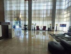 Un vestíbulo amplio con techo alto, ventanas grandes y una recepción.