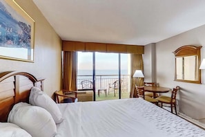 A hotel room with a large bed, a balcony with chairs, a table, and a view of the sea. - The Patricia Grand 0728 (Myrtle Beach)
