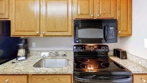 Uma cozinha com armários de madeira, uma pia de aço inoxidável, um micro-ondas preto, um fogão e uma torradeira.