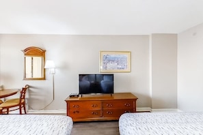 A hotel room with a bed, a TV, a wooden dresser, a desk with a chair, and a framed picture on the wall. - The Patricia Grand 0728 (Myrtle Beach)